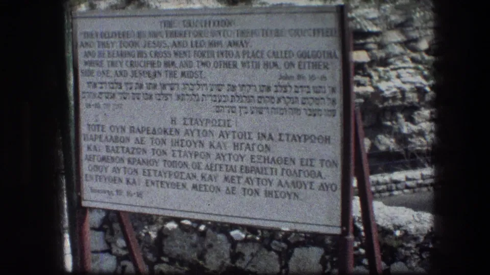 1976 Garden Tomb footage showing the crucifixion description sign, its metal supports, and rough Jerusalem stone surroundings.