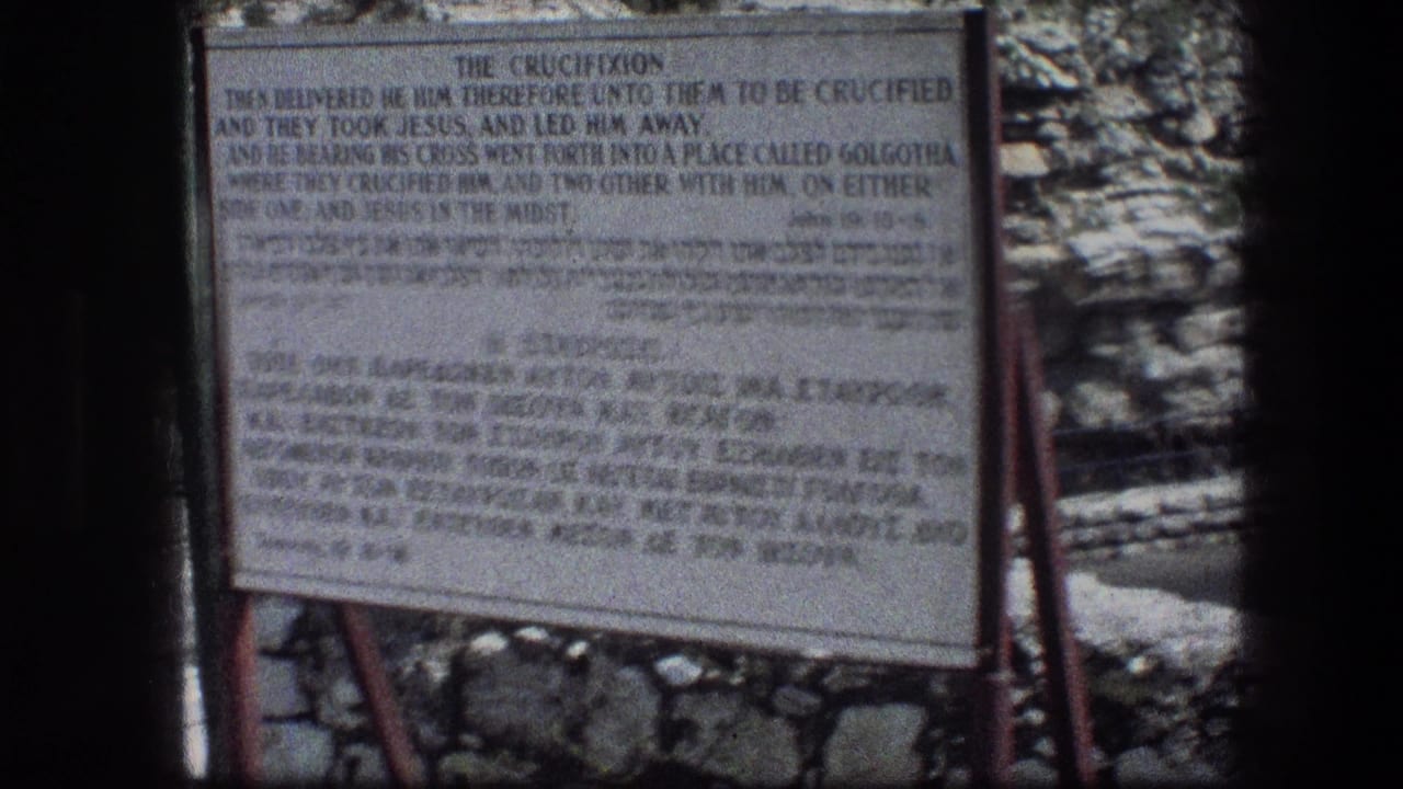 White crucifixion sign with black lettering beside a stone wall.