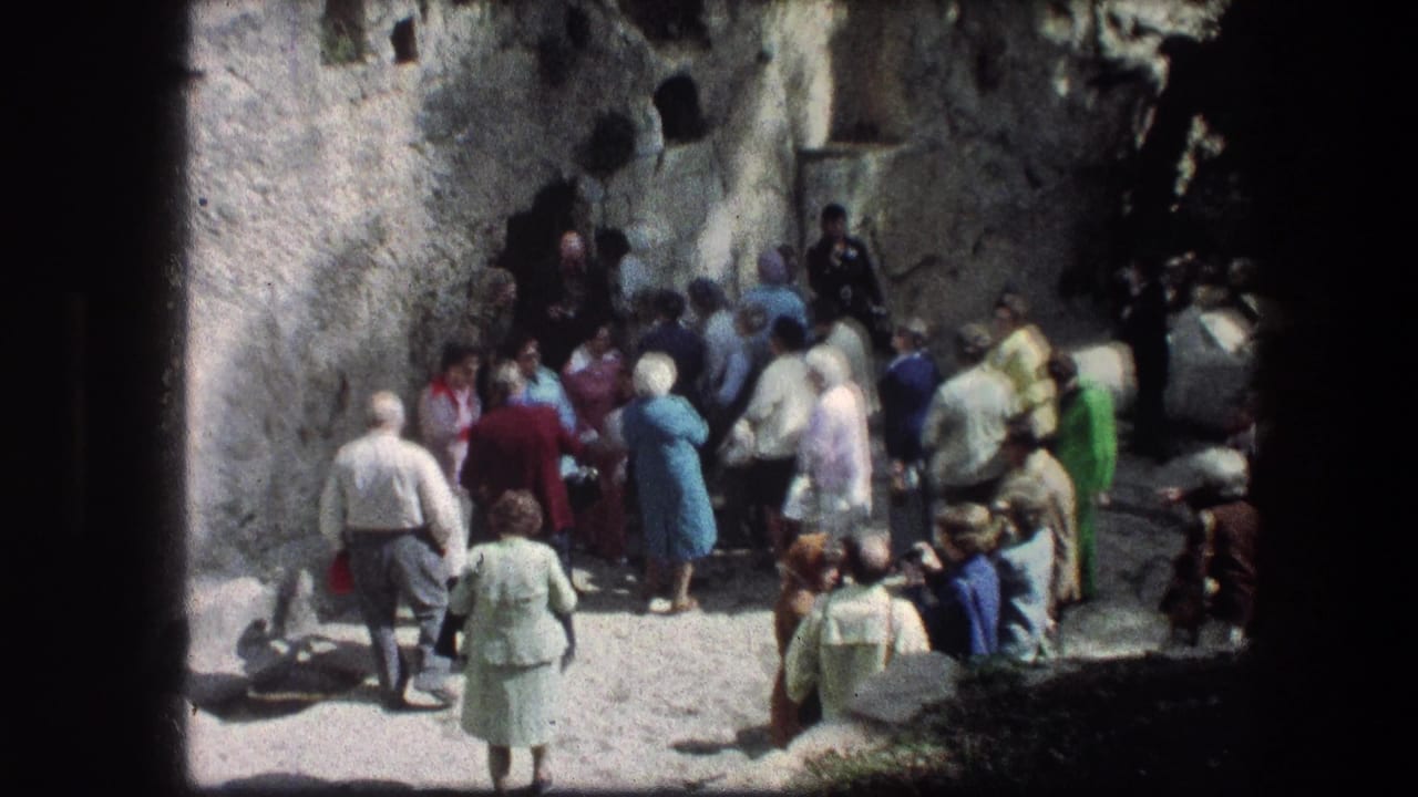A small visitor group moves near the Garden Tomb stone wall in Jerusalem, with soft 8mm focus and bright sunlight.