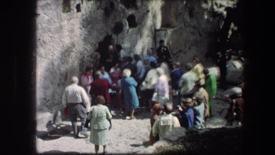 A small visitor group moves near the Garden Tomb stone wall in Jerusalem, with soft 8mm focus and bright sunlight.
