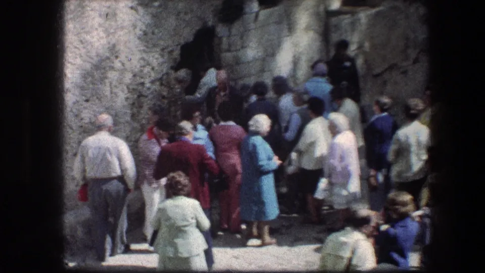 Visitors in 1970s attire gather tightly by a stone opening at the Garden Tomb site in Jerusalem.