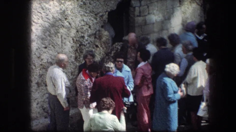 Adults stand in conversation or observation near the Garden Tomb stonework in Jerusalem, with faces partly visible.