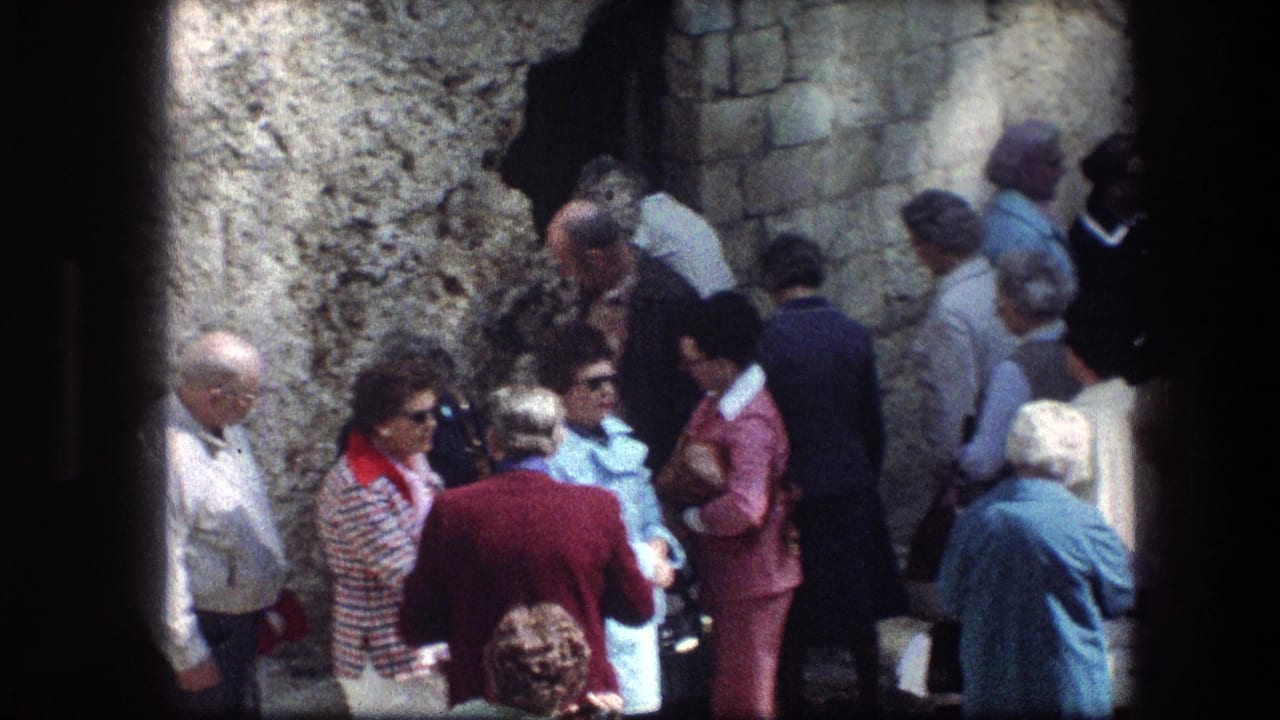 Visitors stand and talk near a rough white stone wall and dark doorway.