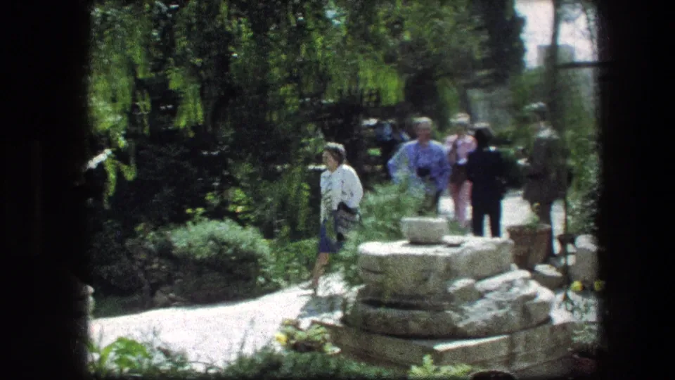 Woman in a white top walks along the Garden Tomb path in Jerusalem with other visitors behind her.