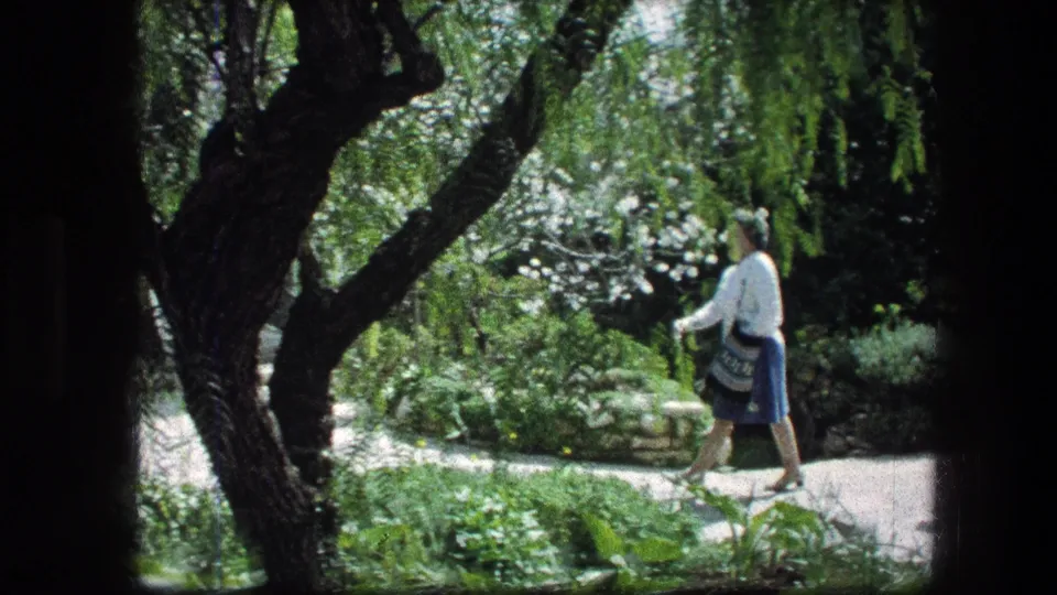 The woman walks beneath trees and past dense plantings in the Garden Tomb grounds in Jerusalem.