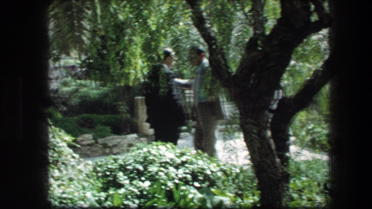 1976 Garden Tomb view with adults standing near stone edging and lush greenery in a shaded Jerusalem garden.