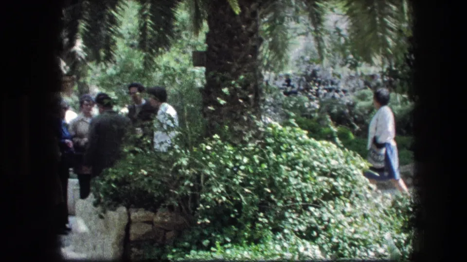 1976 Garden Tomb frame showing adults gathered in conversation and a woman walking through the Jerusalem garden.