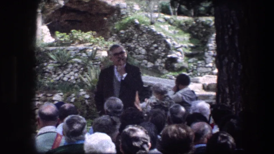 At the Garden Tomb in Jerusalem, a guide in a dark suit speaks to a gathered tourist group near stone paths and garden walls.