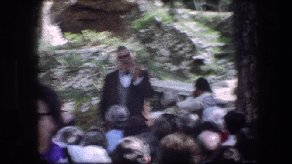 1976 8mm frame from the Garden Tomb area with motion blur as a speaker addresses visitors near stone walls.