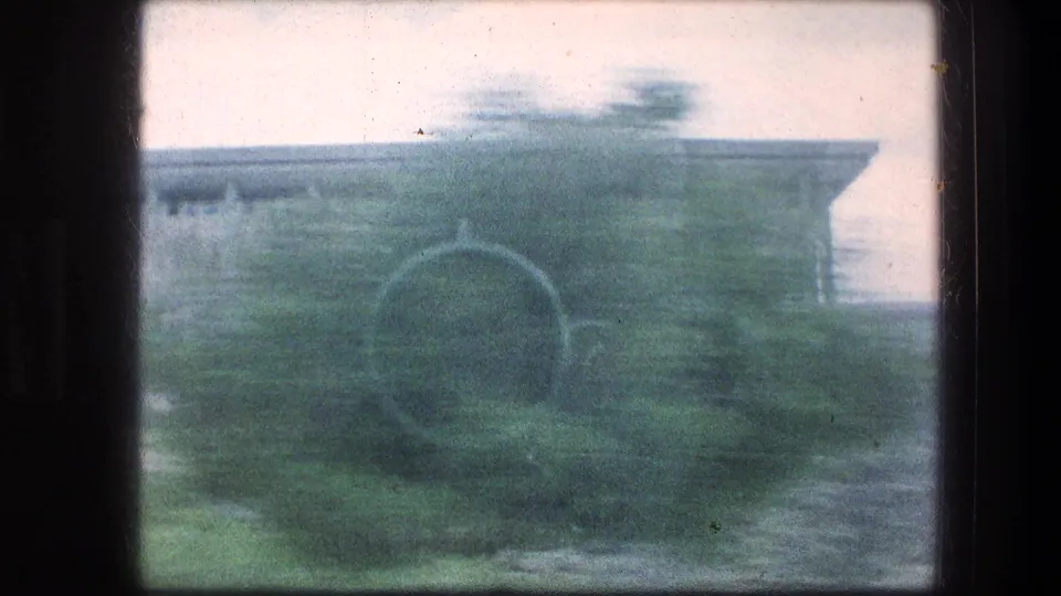 A handheld passing view shows a garden path, greenery, and part of a grey stone structure at the Jerusalem site.
