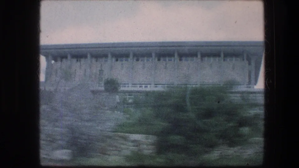 The clip ends on a passing view of a large grey stone structure behind garden plants and a paved approach.