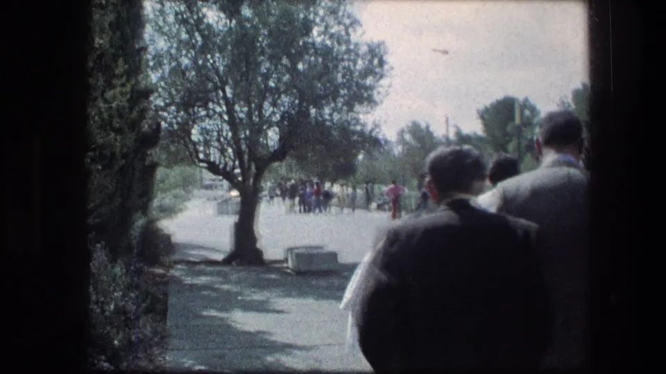 1976 8mm view at the Garden Tomb in Jerusalem showing visitors from behind on a tree-lined pathway.
