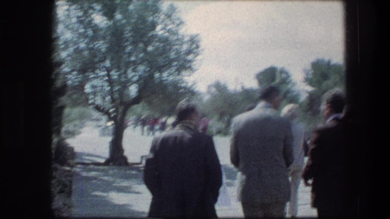 Garden Tomb visitors in 1976 Jerusalem walk along a sunlit avenue framed by trees and dark foreground edges.