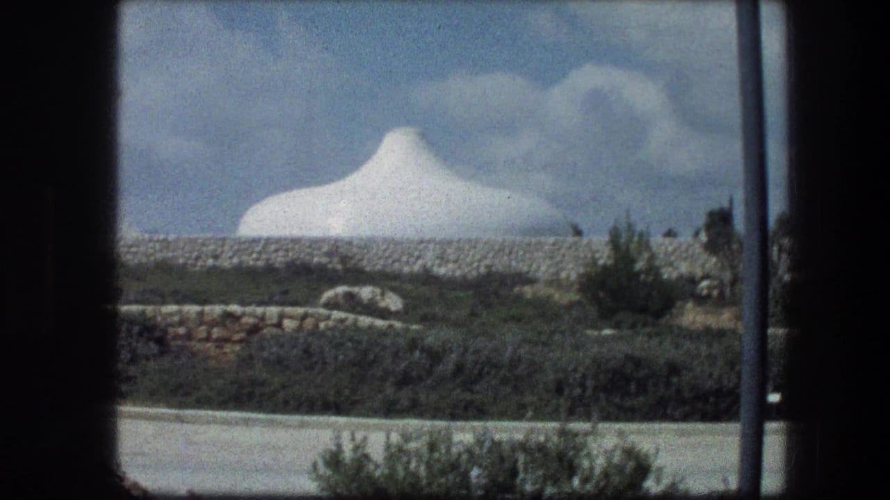 A white domed structure at the Garden Tomb area in Jerusalem appears beyond stone walls and shrubs under scattered clouds.