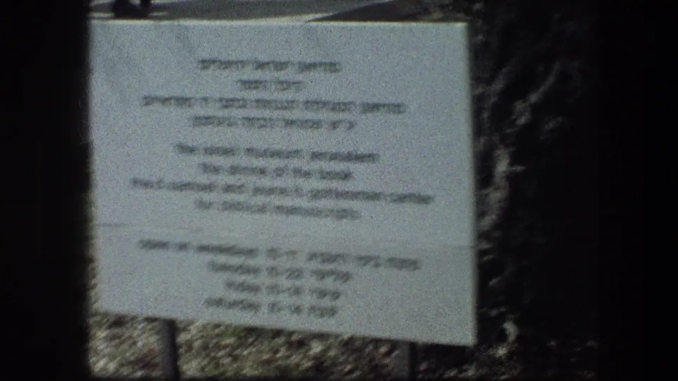 A posted sign at the Garden Tomb area is filmed in soft focus, with surrounding foliage and stonework visible below.