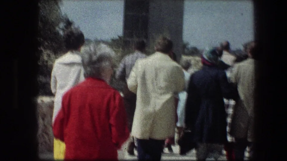 A group of visitors, including a person in a red coat, walks along a sunlit stone path in 1976 Jerusalem travel footage.