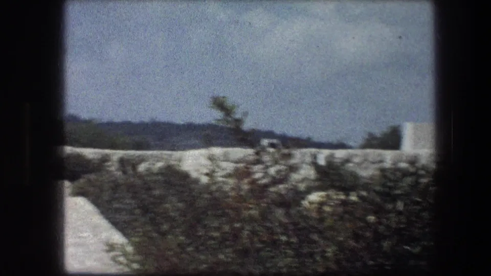 1976 8mm view at the Garden Tomb in Jerusalem, showing greenery, stonework, and a distant white structure.