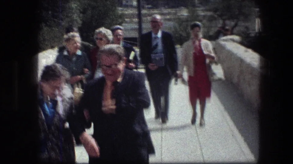 Group of tourists in 1970s attire walking along a stone path at the Garden Tomb in Jerusalem.
