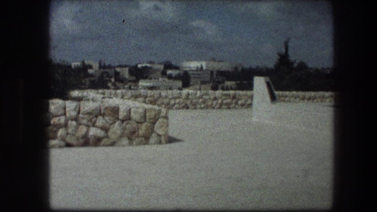Wide view of stone walls, open paving, cloudy sky, and distant buildings beyond the site.
