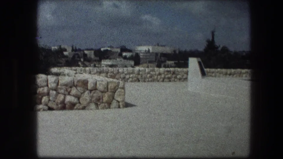 1976 8mm travel frame showing the Garden Tomb site in Jerusalem, with stonework, open paving, distant buildings, and a soft handheld look.