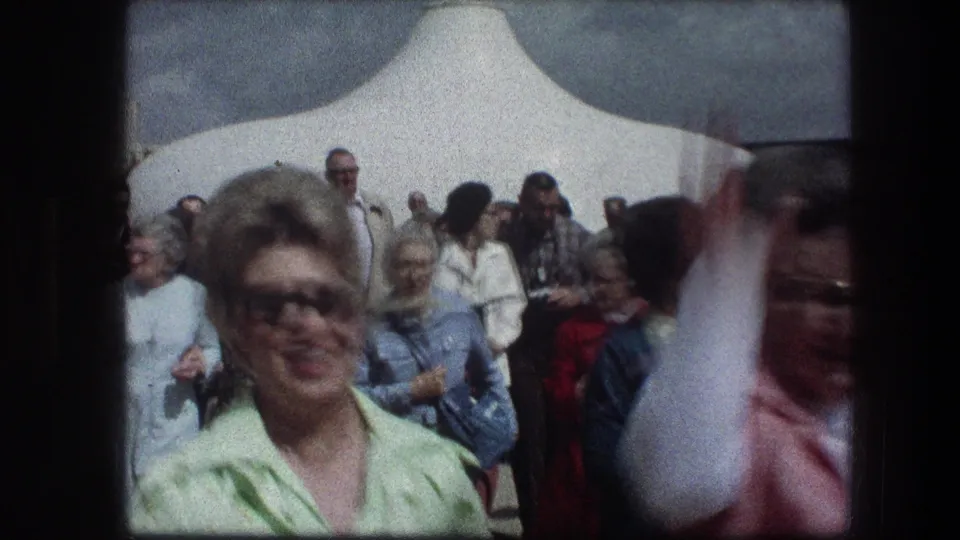 1976 Garden Tomb visitor scene in Jerusalem, showing tourists under a white canopy and a smiling woman in a light green blouse near the camera.