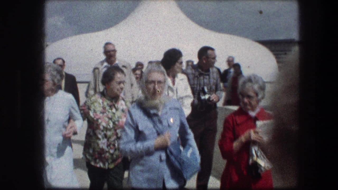 Tourists walking toward the camera near a white structure outdoors.