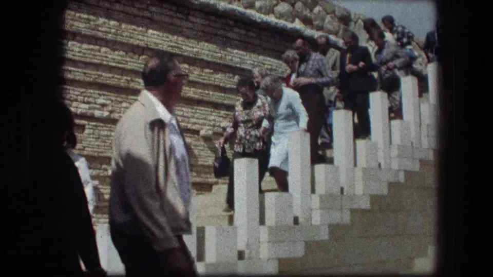 Visitors descend the white stone steps at the Garden Tomb in Jerusalem, with a stone wall and bright sky visible.