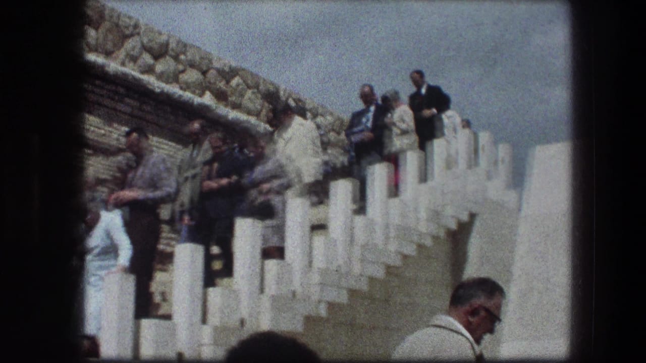 Older visitors stand and descend white-railed stone steps beside a stone wall.