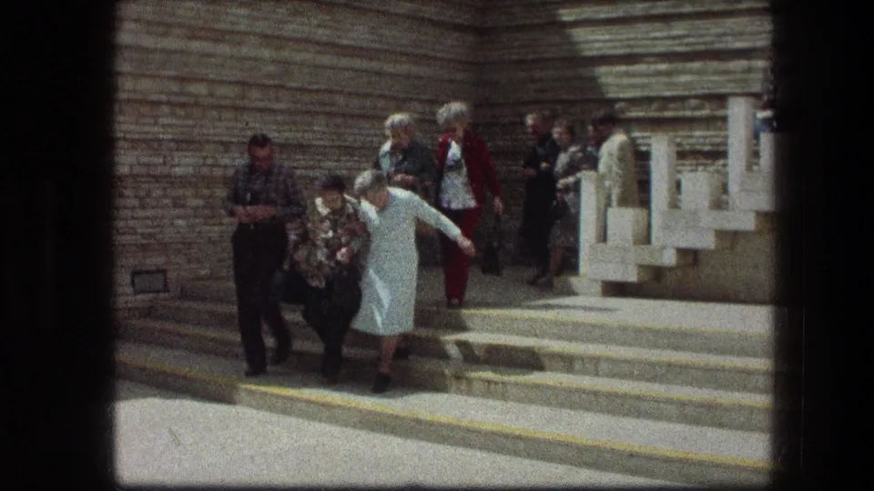 Visitors in 1970s clothing assist older women down broad stone steps at the Garden Tomb in Jerusalem.