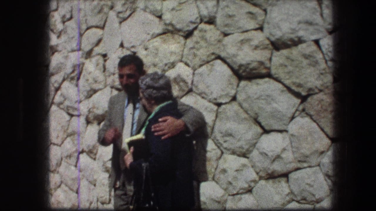 At the Garden Tomb in Jerusalem, a man in a light suit stands with an older woman in a dark coat against a stone wall.