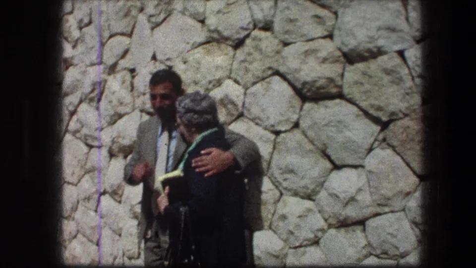 At the Garden Tomb in Jerusalem, a man in a light suit stands with an older woman in a dark coat against a stone wall.