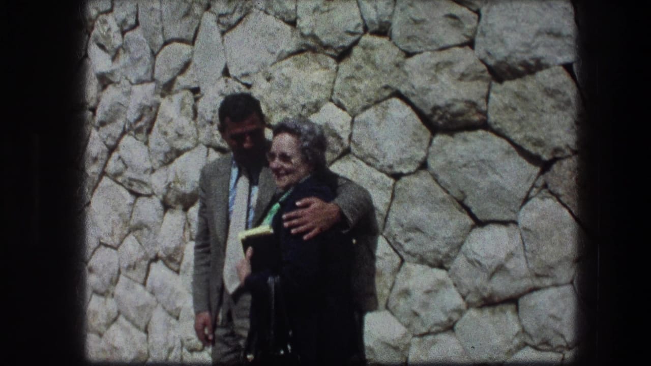 Smiling older woman stands beside a man with his arm around her.