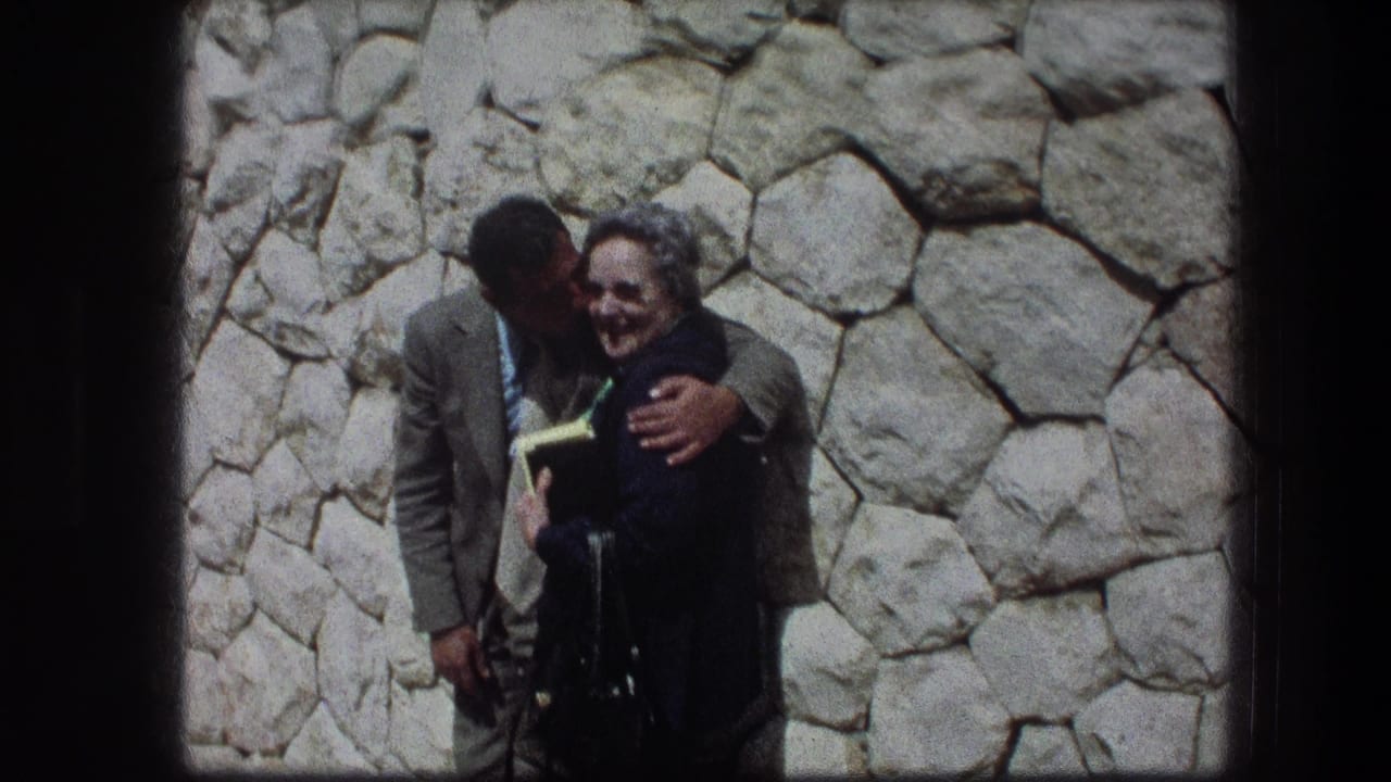 Young man and woman embracing in front of a pale stone wall.