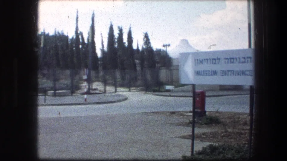 Roadway and entrance sign near the Garden Tomb in Jerusalem, with tall trees and soft 1970s 8mm color.