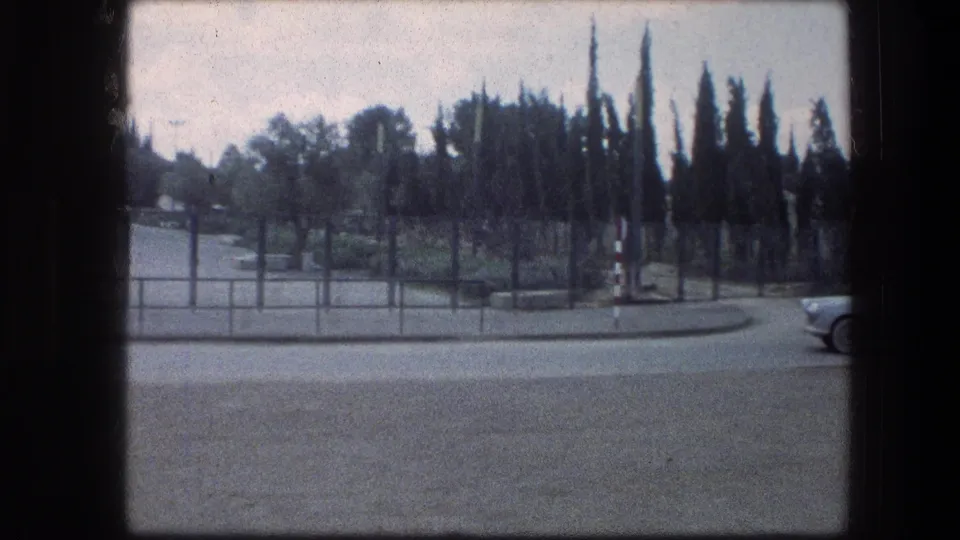 Garden Tomb roadside entrance area in Jerusalem, with trees, fencing, a paved road, and a partial car at the frame edge.