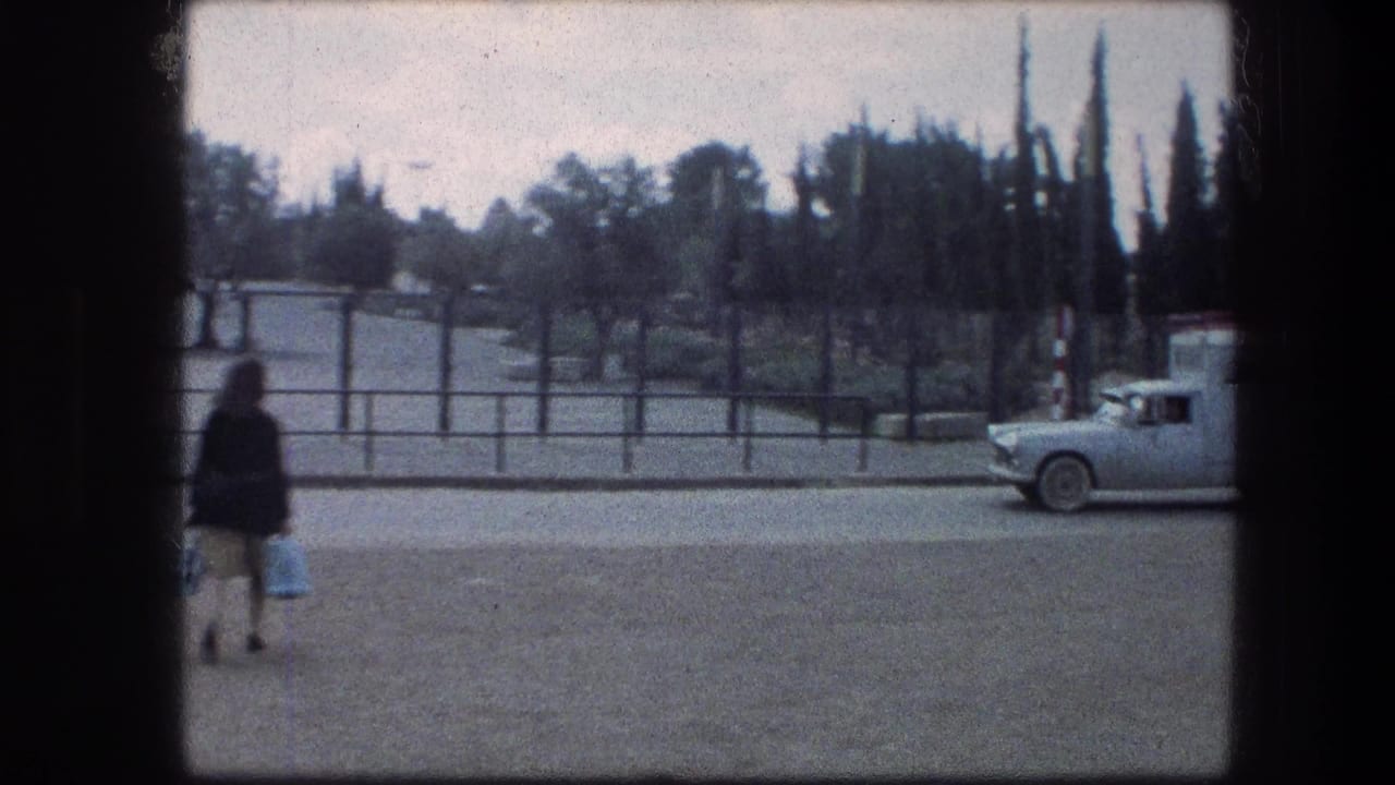 1976 home-movie frame near the Garden Tomb in Jerusalem, with a woman carrying bags and a light truck partly entering the roadside view.