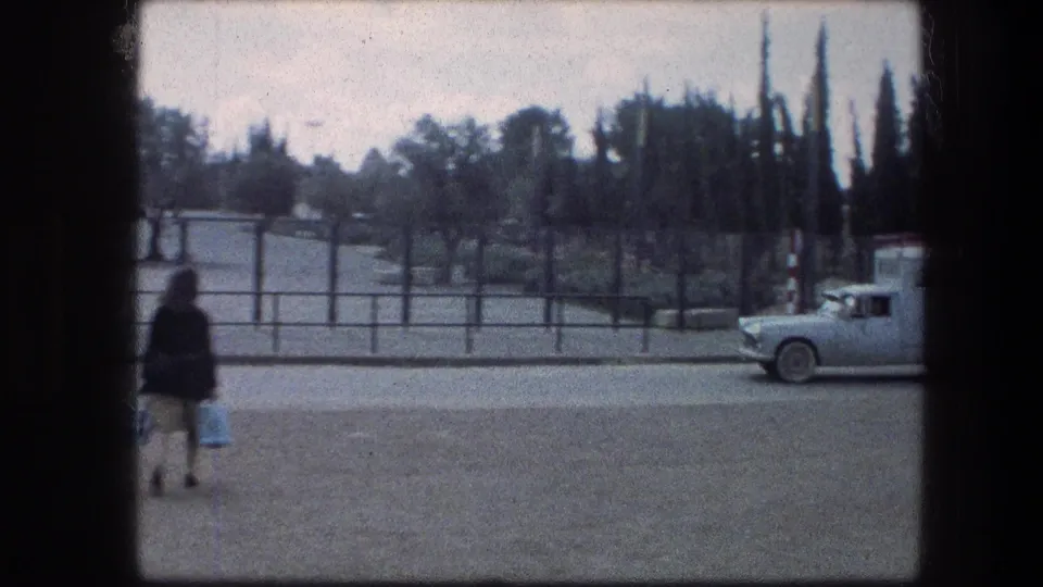 1976 home-movie frame near the Garden Tomb in Jerusalem, with a woman carrying bags and a light truck partly entering the roadside view.