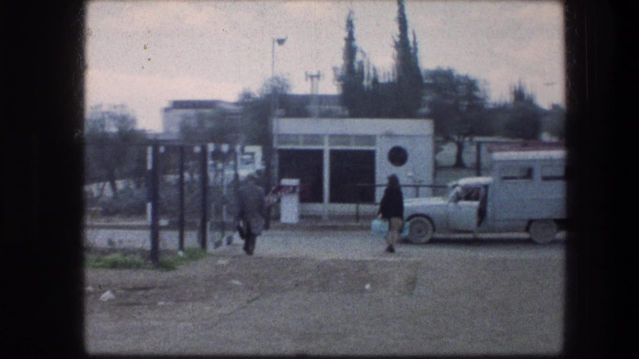 Gate area with pedestrians, a small white structure, and a parked light-colored car.