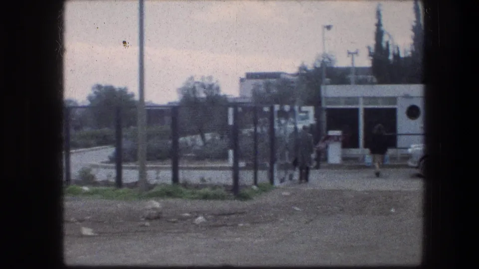Garden Tomb area in Jerusalem, 1976, with distant visitors walking near a fence and a small white building beside a road.