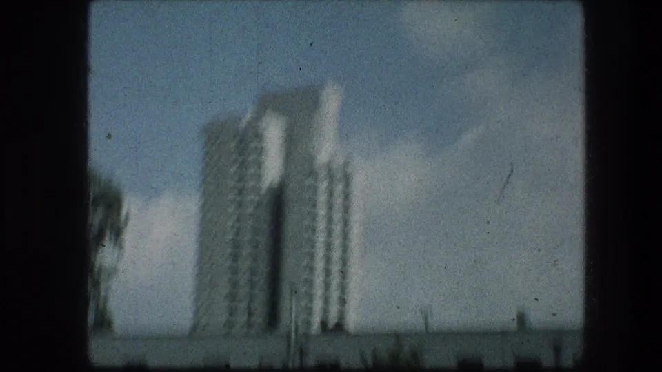 Final 1976 Jerusalem-area frame with the tower blurred by vehicle movement, set above a low wall and pale sky.