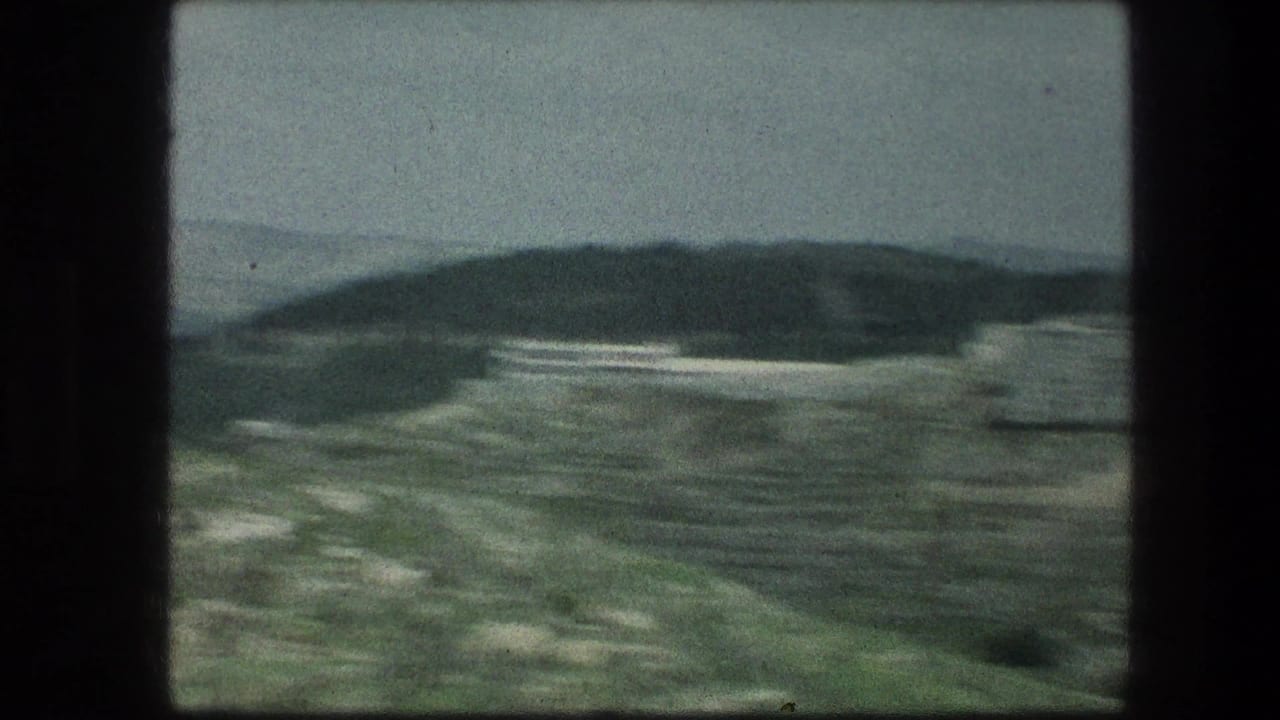 Rocky hillside and distant hills beneath a gray sky.