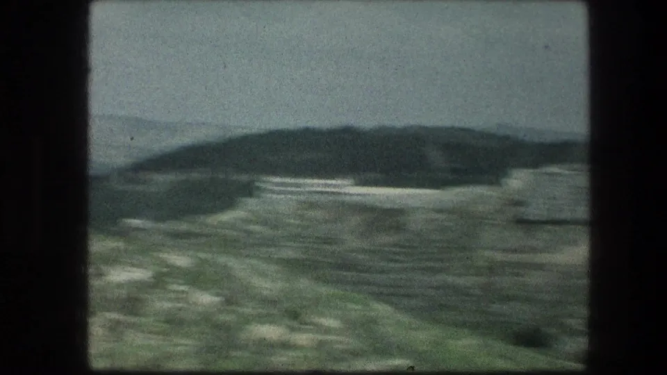 1976 8mm view near the Garden Tomb in Jerusalem, showing rough ground, sparse grass, and distant hills under a gray sky.