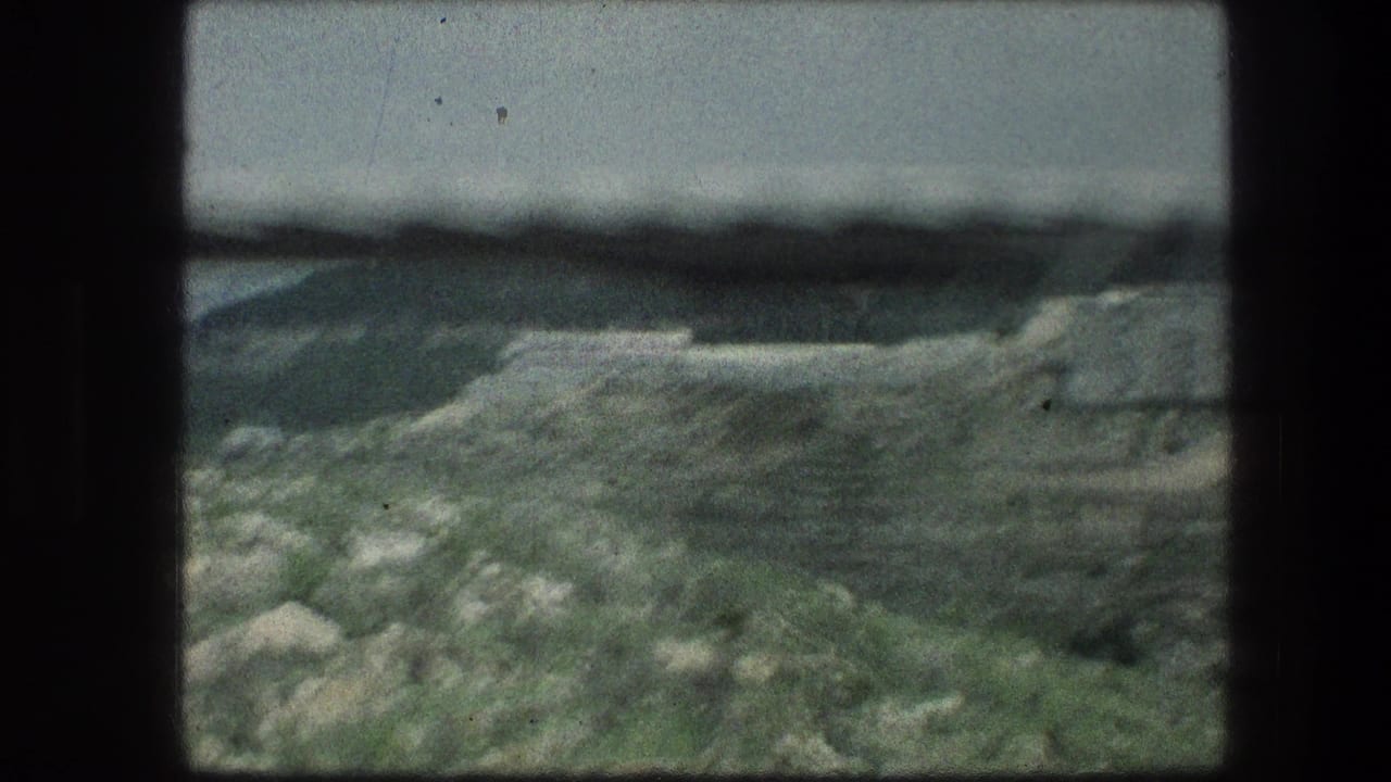 Rock-strewn slope with pale grass and a low hill beyond.