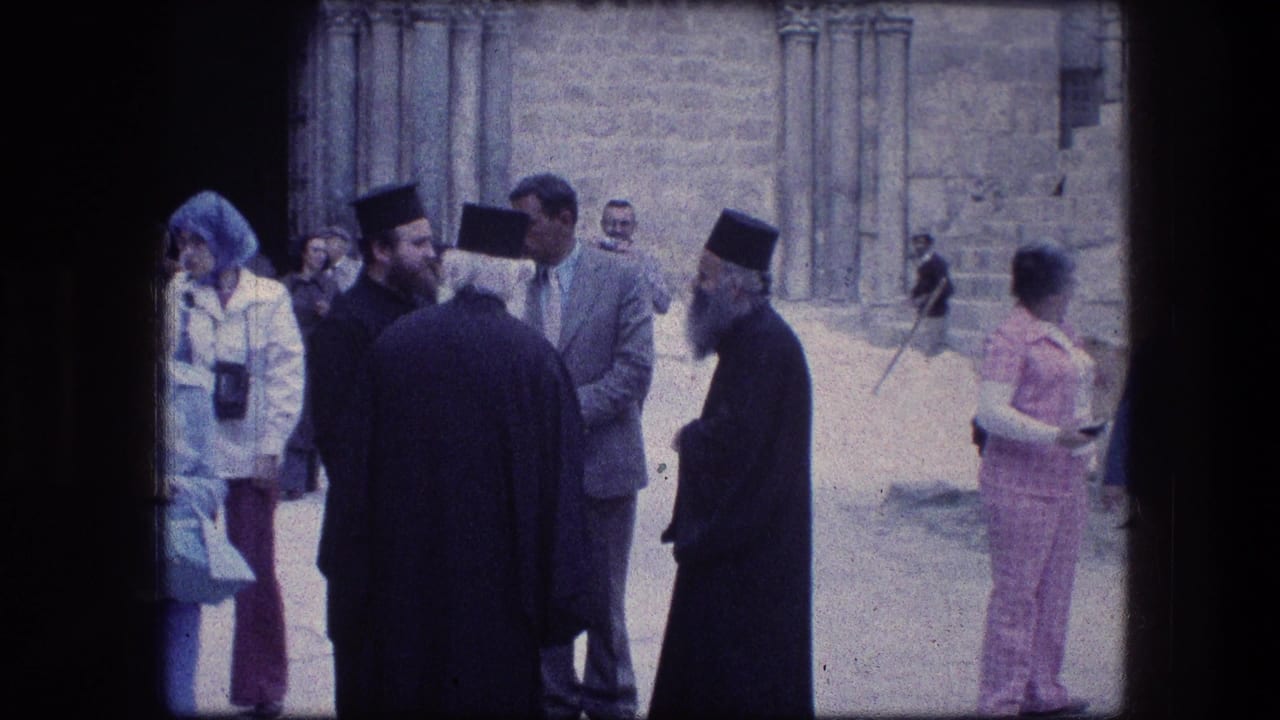 Orthodox monks in black robes speak with visitors near stone columns.