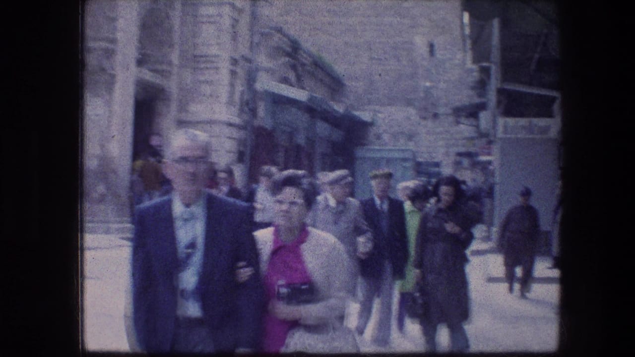 1976 home-movie view of adults in suits, coats, and dresses walking along a narrow Jerusalem stone street.