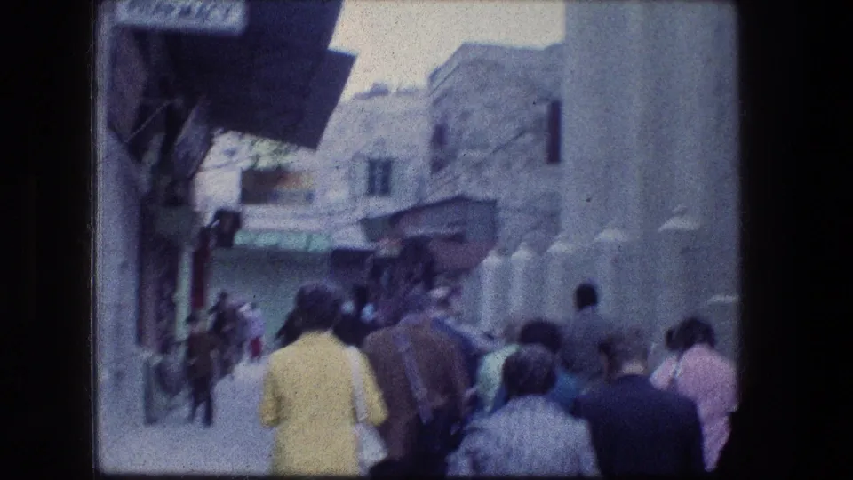 Handheld 8mm view of pedestrians moving away through a narrow stone street in Jerusalem in 1976.