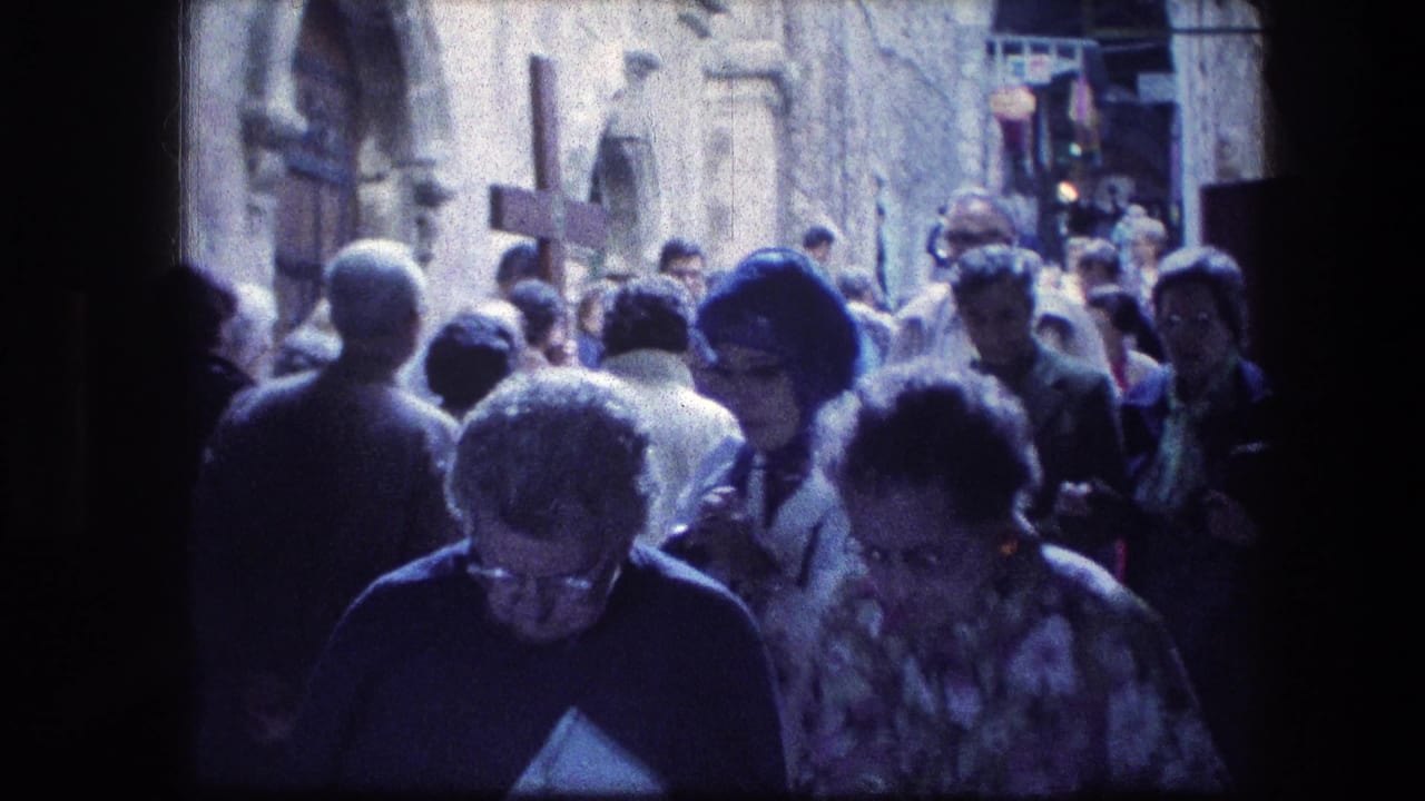 Crowd of adults walking along a stone alley, with several faces visible near the camera.