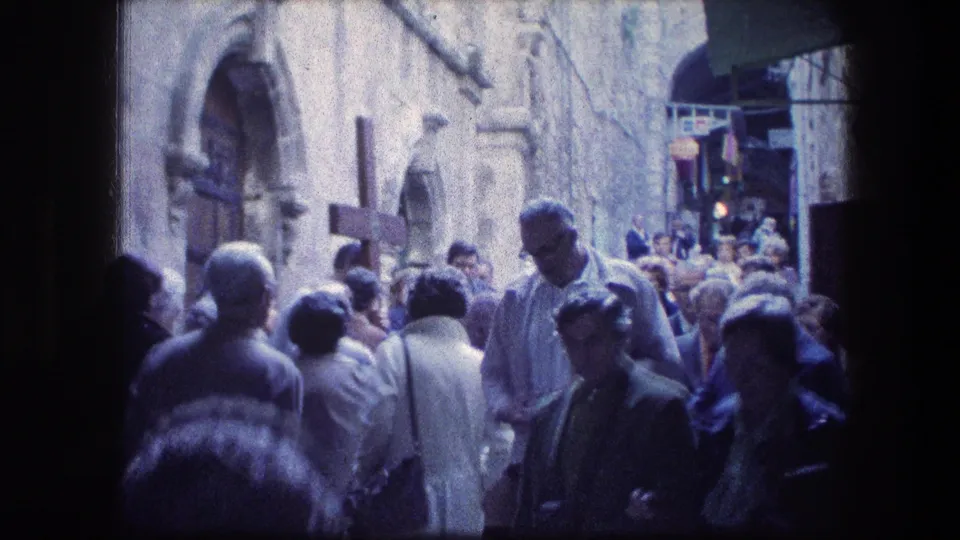 A crowded 1976 Garden Tomb walkway shows adults moving through stone architecture under mixed shadow and daylight.