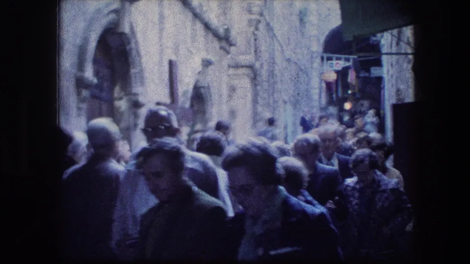 End frame of a 1976 8mm Jerusalem Garden Tomb crowd scene, with visitors passing near the camera in a narrow alley.