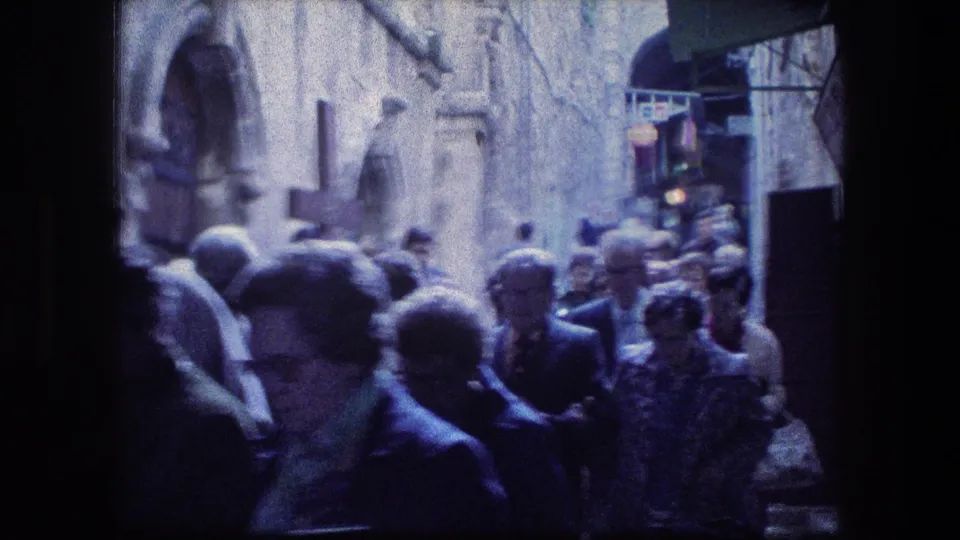 1976 8mm view near the Garden Tomb in Jerusalem, showing pedestrians in a crowded stone alley with soft blue-tinted film color.